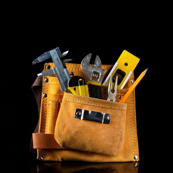 A tool belt with a wrench, pliers, measuring stick, leveler, and other tools sticking out of the top.