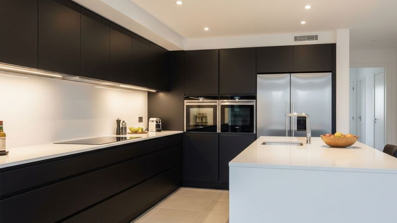 A sleek, contemporary kitchen with dark matte high-quality kitchen cabinetry and light countertops.