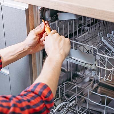 repair technician using screwdriver on dishwasher