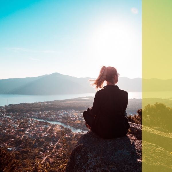 A woman sitting on a beach looking over a lake