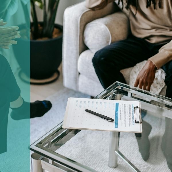 A therapist and a patient sit in a room, an evaluation sheet sits on the table between them