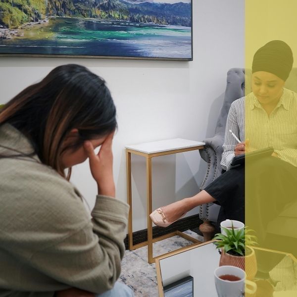 A therapist takes notes while a client looks upset on the couch across from her