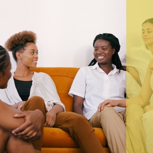 A group of young women sit together on a coach, smiling