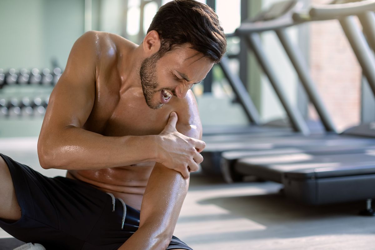 A male athlete suffering from chronic muscle pain at the gym.
