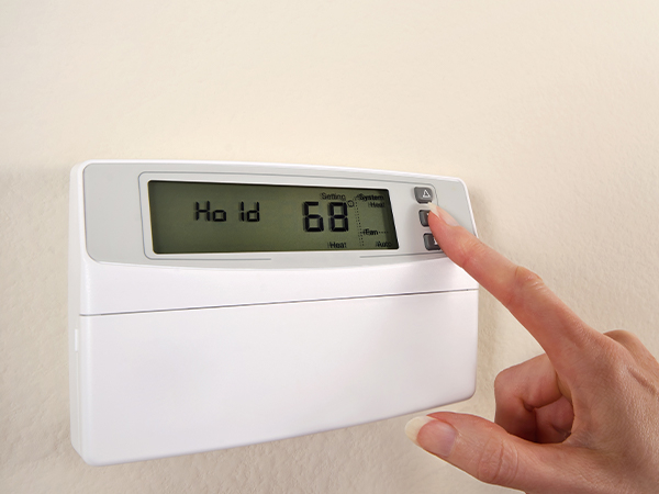  Woman’s hand adjusts thermostat set at 68, display reads “Hold.”