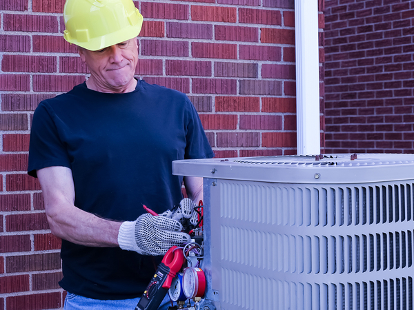 HVAC Technician diagnoses outdoor air conditioning condenser with tools and gauges.