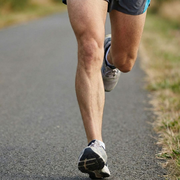 A close-up of a runner's calves and feet in mid-stride on an asphalt path.