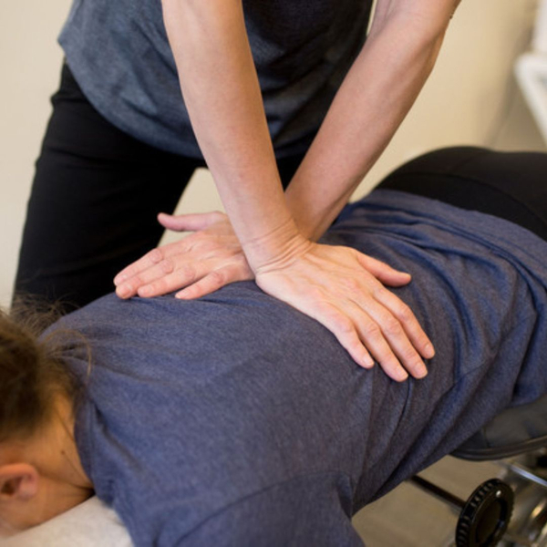 A chiropractor performs a spinal adjustment on a patient's upper back on a treatment table.