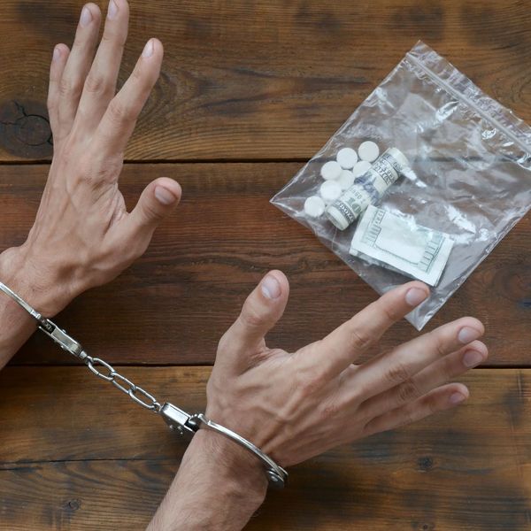 a person in cuffs in front of a bag of money and pills