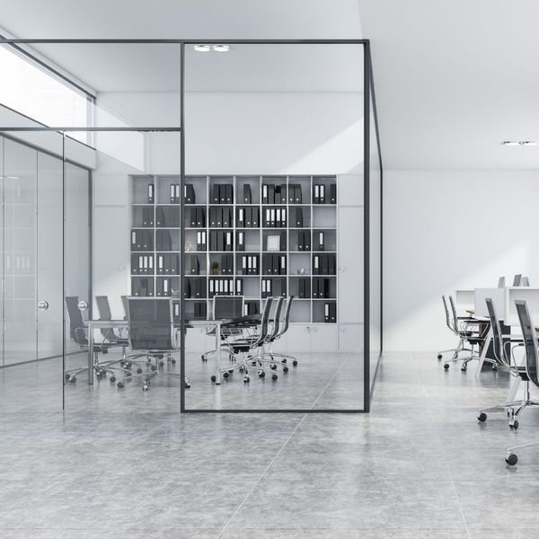 A minimalist office with a black-framed glass partition enclosing a meeting room with white shelves full of binders.