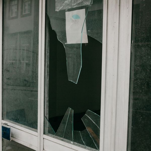 A broken window pane with several large, sharp shards of glass remaining in the white frame.