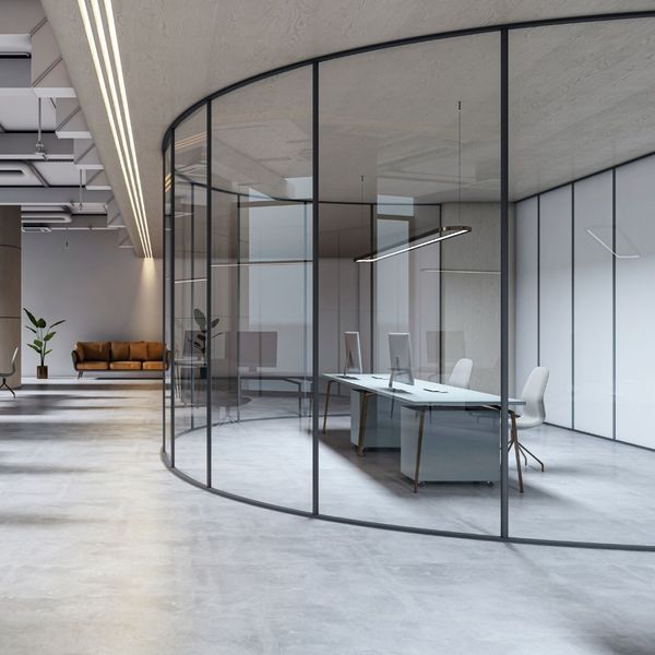 An open-plan office featuring a gracefully curved glass partition wall that encloses a modern workspace.