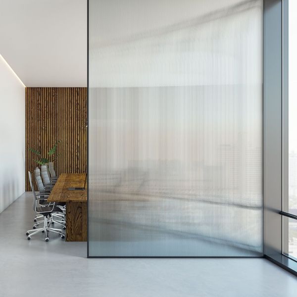 A modern office meeting room separated by a full-height fluted glass partition, with a wooden conference table visible.