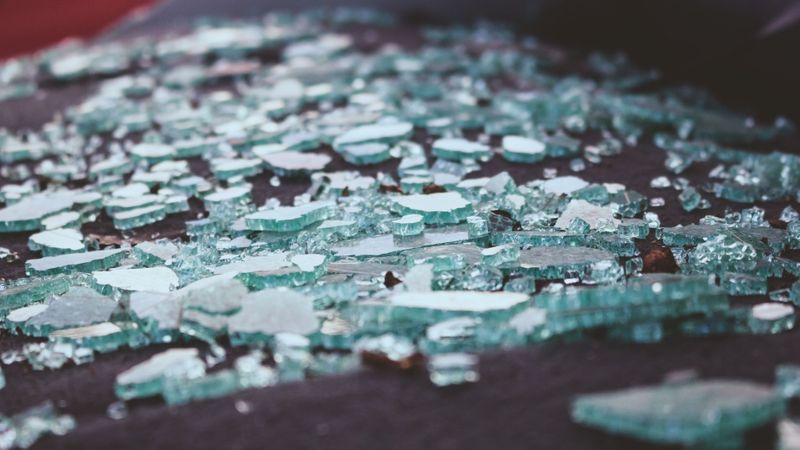 A close-up, artistic shot of shattered tempered glass pieces scattered across a dark surface.  A close-up, artistic shot of shattered tempered glass pieces scattered across a dark surface.