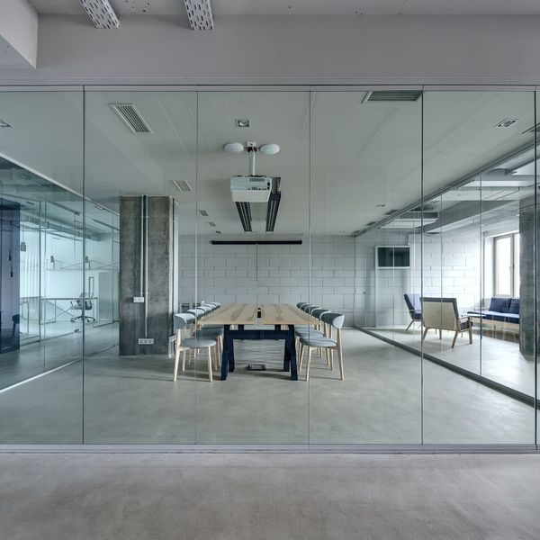 Large open plan office or meeting room enclosed by clear glass partitions, featuring a long wooden conference table with chairs, and a projector.