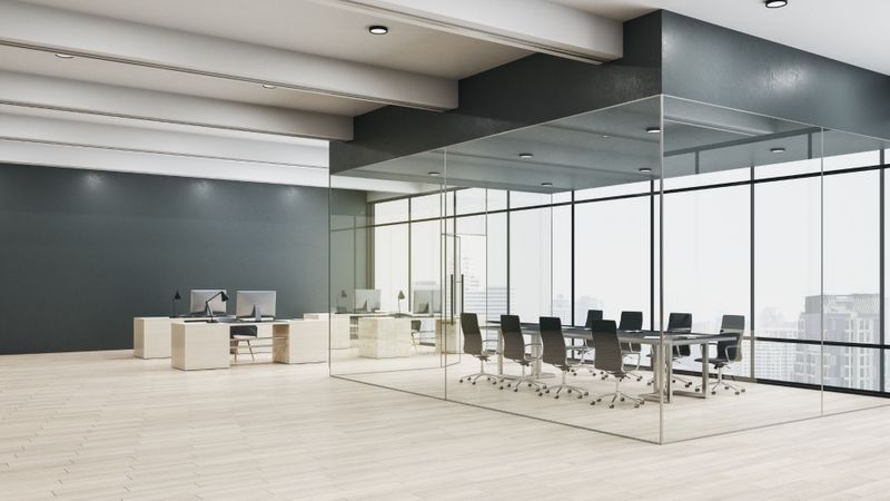 A spacious, modern open-plan office with a central glass-walled conference room overlooking a city skyline through large windows. A spacious, modern open-plan office with a central glass-walled conference room overlooking a city skyline through large windows.