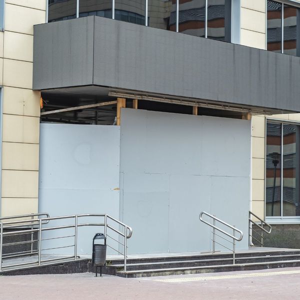 The entrance of a commercial building temporarily secured with large grey boards after a glass emergency.