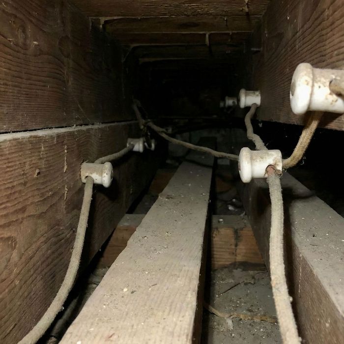 A close-up view of dusty, outdated knob-and-tube wiring between wooden joists in an old building.