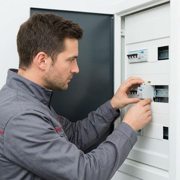 A professional electrician in a grey uniform carefully installing a new circuit breaker into a modern panel.
