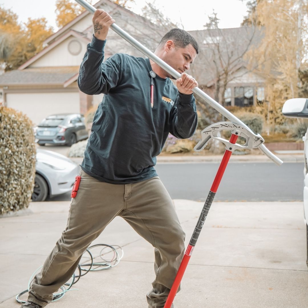 electrician using a manual conduit bender to shape a metal pipe on a residential driveway