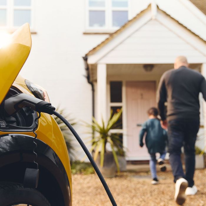 yellow electric car charging in front out house