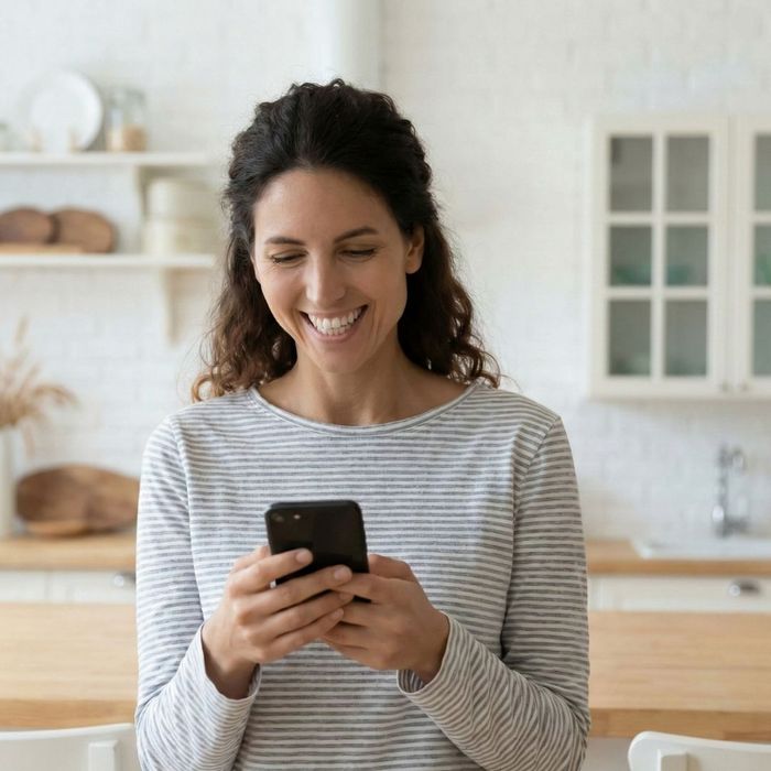 A happy homeowner smiles while using her smartphone in a modern kitchen.