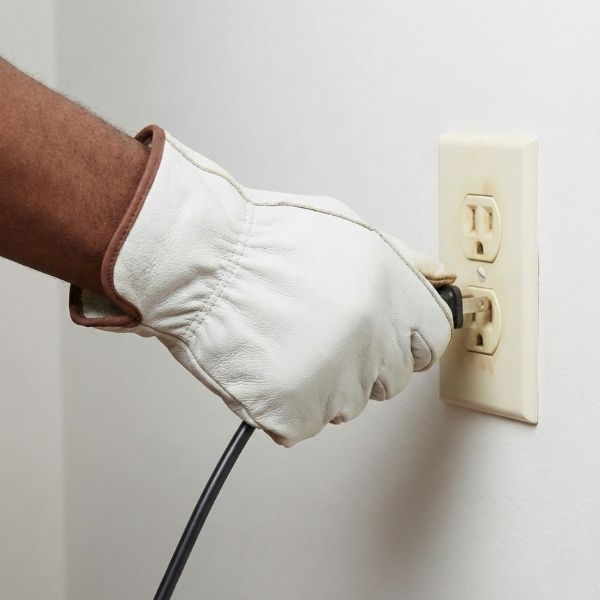 A gloved hand unplugging a cord from an electrical outlet that shows brown burn marks and discoloration.