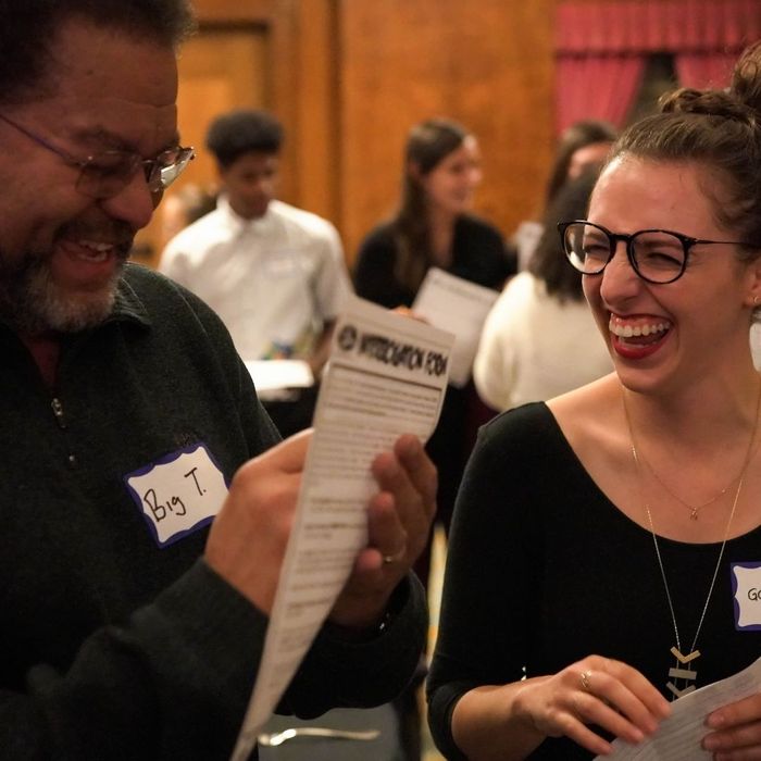 A man and a woman, both wearing name tags, are laughing and studying a document labeled "Interrogation Form" at an immersive true crime dinner event. A man and a woman, both wearing name tags, are laughing and studying a document labeled "Interrogation Form" at an immersive true crime dinner event.