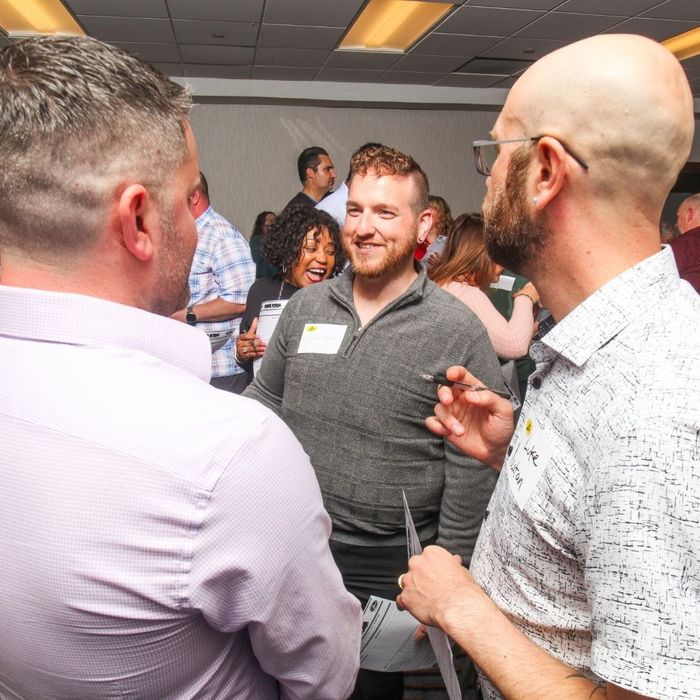 Three guests, including a laughing woman in the background, interacting and discussing clues with a pen and paper at an immersive murder mystery dinner event. Three guests, including a laughing woman in the background, interacting and discussing clues with a pen and paper at an immersive murder mystery dinner event.