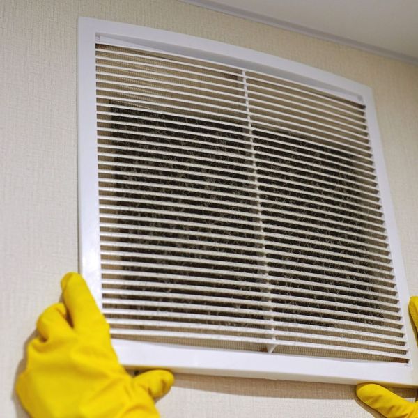 Closeup of someone with rubber gloves removing an air vent cover on a wall