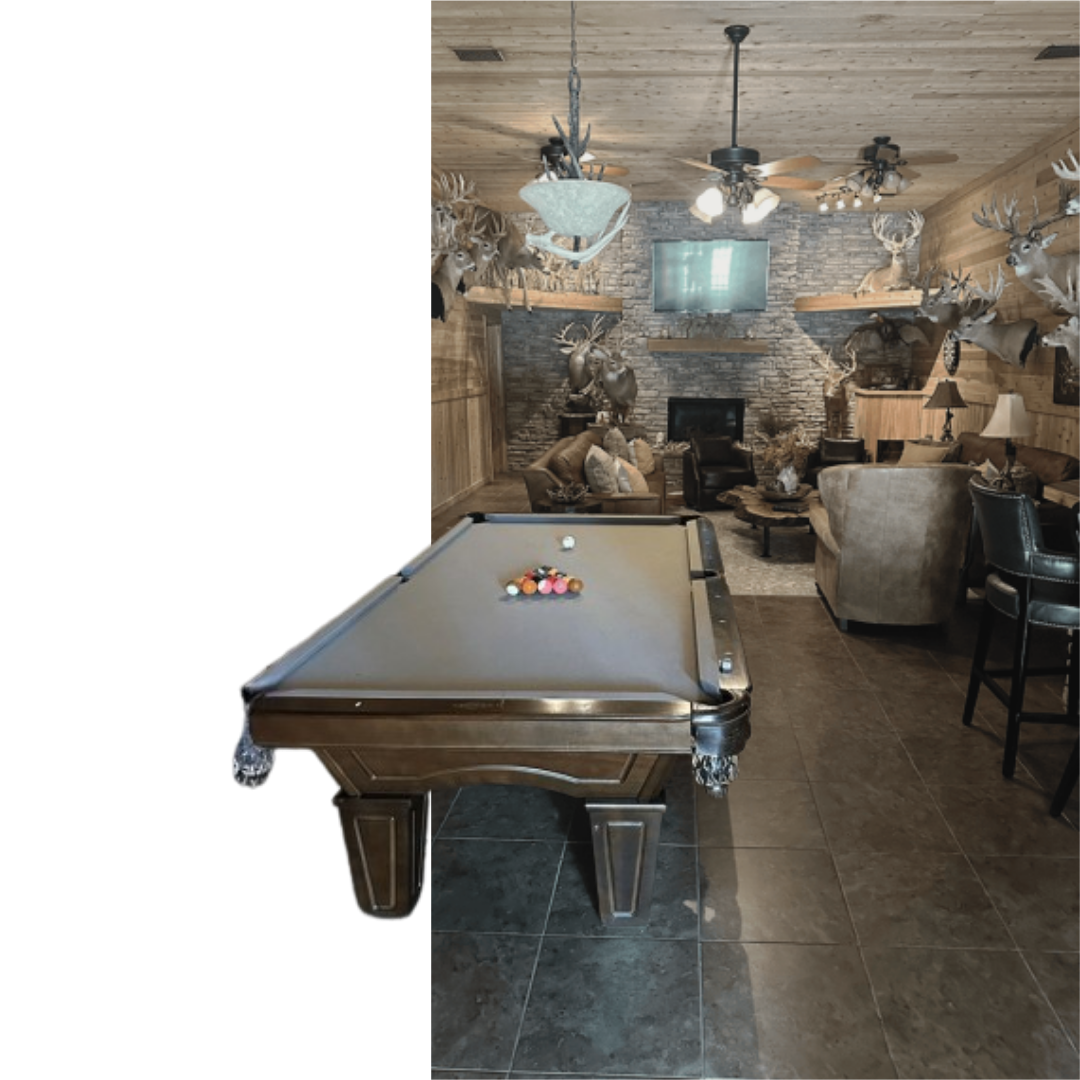 lodge featuring a professional billiard table, plush leather seating, a stone fireplace, and numerous trophy whitetail deer mounts on wood-paneled walls.