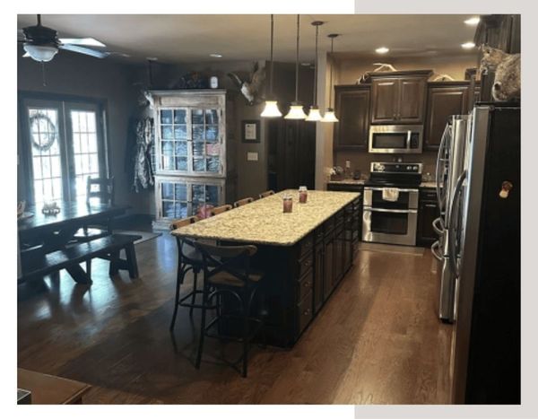A high-end lodge kitchen and dining area featuring a large granite island with barstools, modern stainless steel appliances, and a rustic wooden dining table.