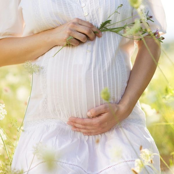 A pregnant woman holding her stomach and flowers.