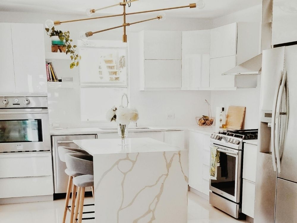 Bright, all-white contemporary kitchen with high-gloss cabinets, a waterfall marble island, and a geometric gold light fixture.