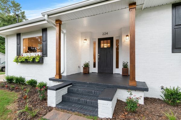 Front exterior of a home with freshly painted white brick, a bold black front door, and natural wood porch pillars.