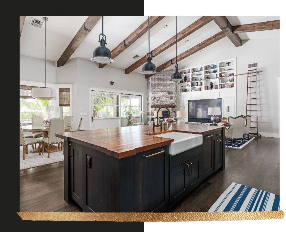 Large open-concept living area featuring a rustic butcher block kitchen island with a farmhouse sink, exposed wood ceiling beams, and a brick fireplace.