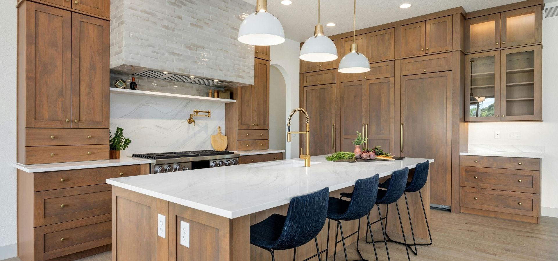 Luxury kitchen featuring custom floor-to-ceiling wood cabinetry, a massive white quartz island with a gold gooseneck faucet, and white dome pendant lights.
