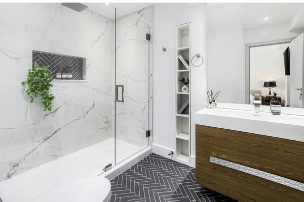 Detailed view of a modern bathroom featuring a dark grey herringbone tile floor, marble wall slabs, and a custom recessed shower niche.