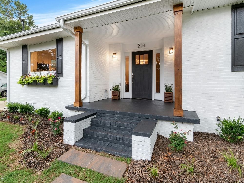Front exterior remodel with freshly painted white brick, a bold black front door, matching black shutters, and natural wood porch columns.