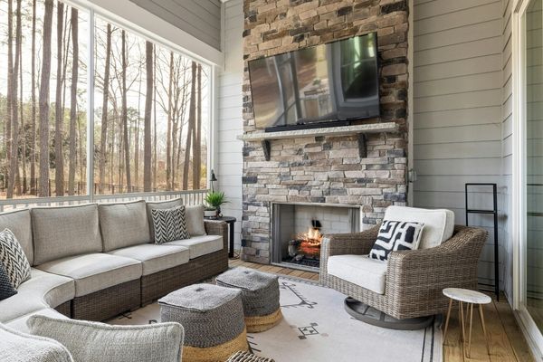 Cozy screened-in porch featuring a floor-to-ceiling stacked stone fireplace with a rustic wood mantel and mounted television.