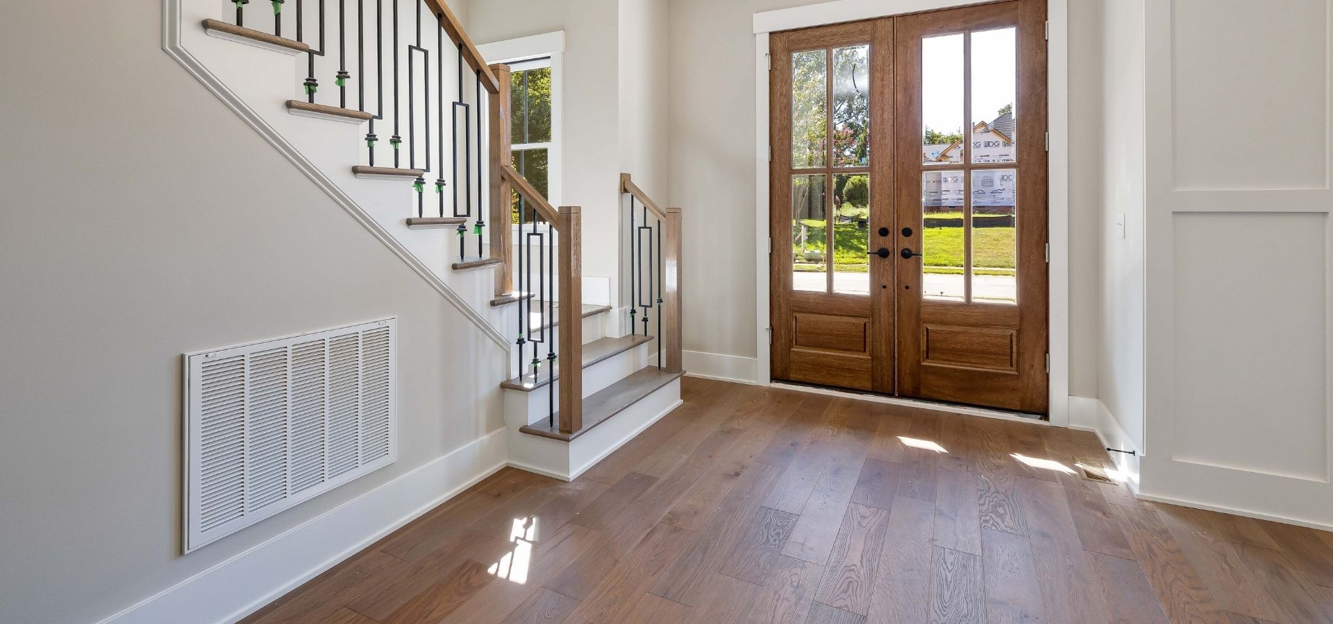Elegant home entryway showcasing professionally installed wide-plank oak hardwood floors and a set of double wood-and-glass front doors.