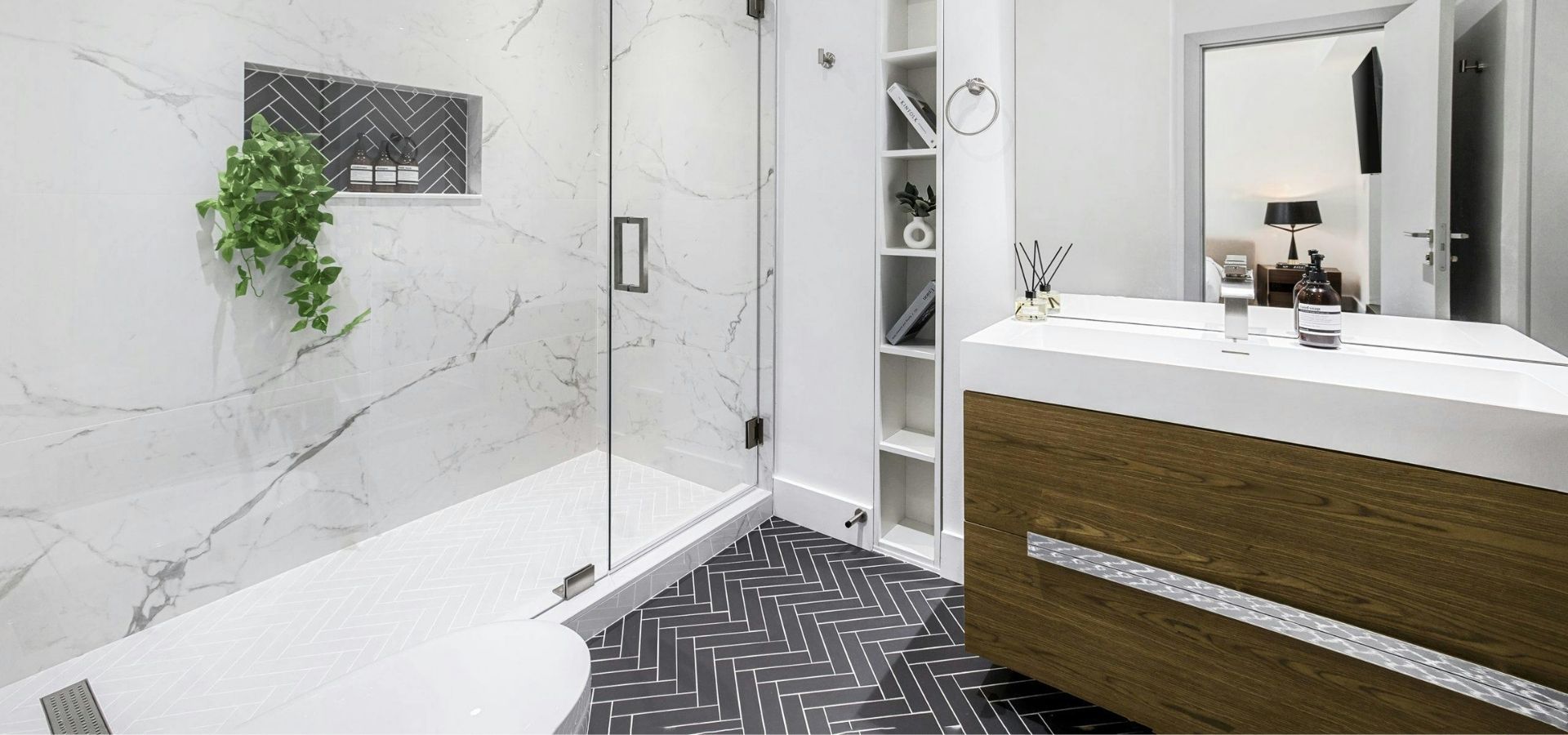 Modern bathroom remodel featuring a walk-in glass shower with white marble wall tile and dark grey herringbone floor tile.