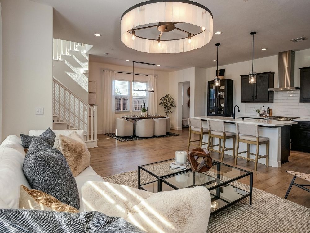 Open-concept main floor showing a seamless transition between a modern kitchen with dark cabinetry and a bright, airy living room with warm hardwood floors.