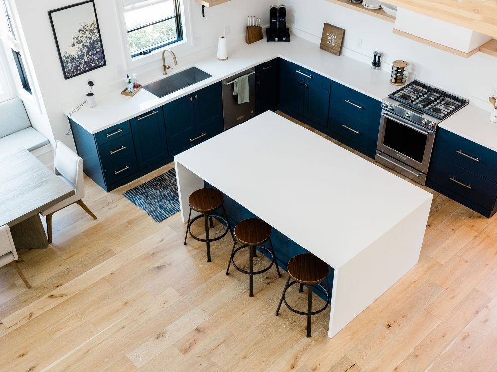 Overhead view of a modern kitchen featuring professionally installed wide-plank light oak hardwood flooring and navy blue cabinetry.
