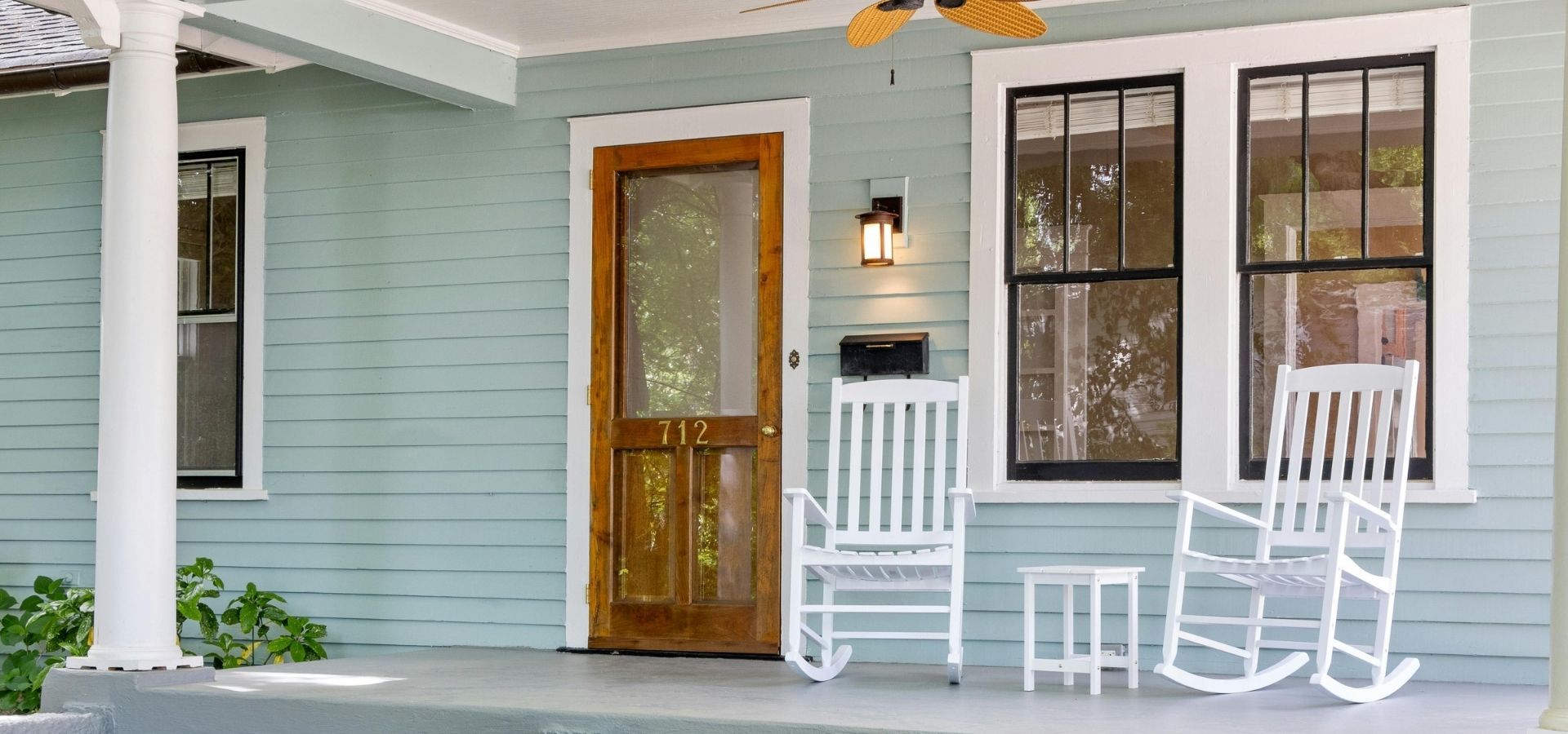 Refreshing home exterior with light sage green siding, crisp white window trim, and a warm natural wood front door on a classic covered porch.