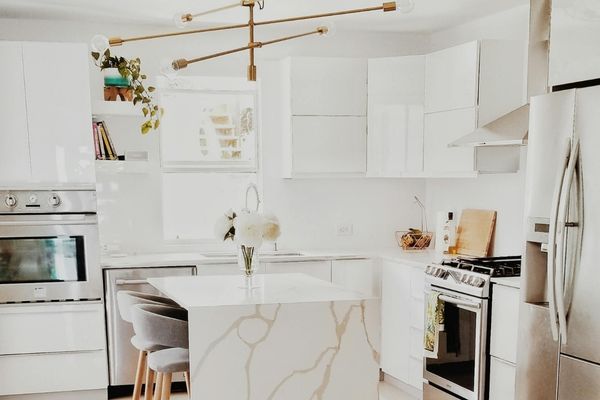Modern minimalist kitchen with high-gloss white cabinetry, a waterfall marble island, and a contemporary gold branch chandelier.