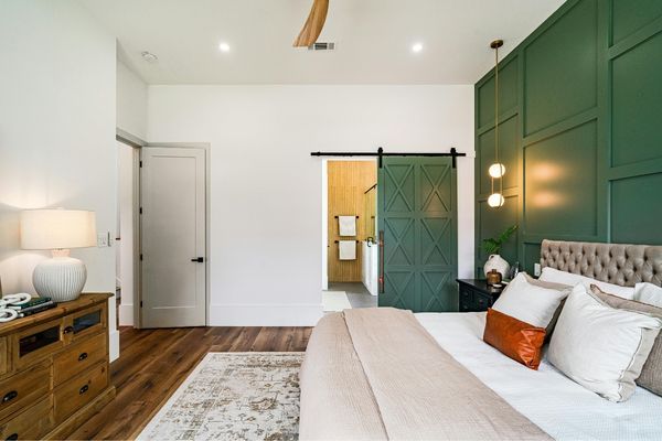 Master bedroom featuring a deep forest green accent wall with custom wood paneling (wainscoting) and a matching sliding barn door.