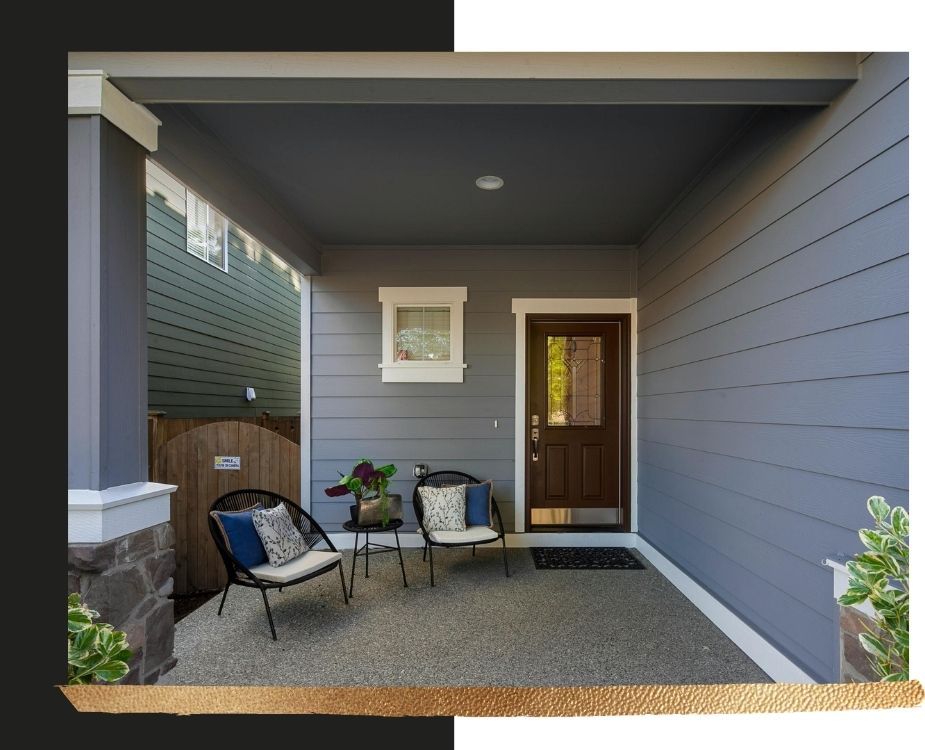 Modern porch entryway featuring slate blue siding, a dark grey painted ceiling, and a rich wood-grain door with stone pillar accents.