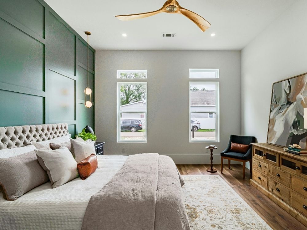 Bright master suite showcasing a custom forest green board-and-batten accent wall, light grey walls, and a natural wood ceiling fan.