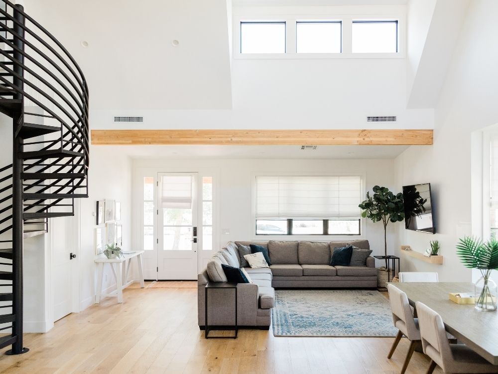 High-ceiling living room featuring a dramatic black spiral staircase, light oak hardwood floors, and a large natural wood support beam.